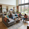 Commercial dormitory common area furniture featuring a spacious grey U-shaped sectional sofa next to large floor-to-ceiling windows