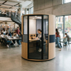 Cylindrical acoustic study pod providing a private, quiet workspace for a student with a laptop in a bustling library atrium