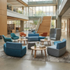 Contemporary higher ed lounge featuring modular blue and grey soft seating, high-back chairs, and round wooden tables on a patterned rug.