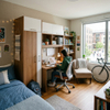 University student desk with wardrobe featuring warm wood tone finish, integrated upper cabinet storage, pinboard, and ergonomic study chair in a dorm room